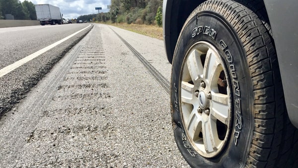 Where should you park when you need help after your tire suddenly deflates while driving on a highway?